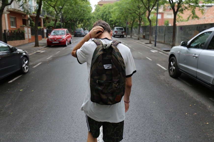 Boy with backpack walking down the middle of the street