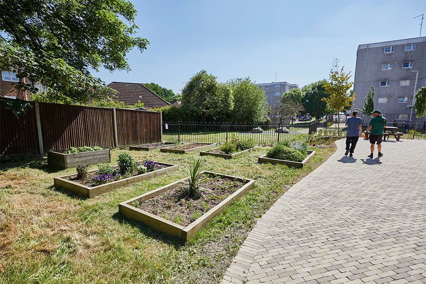 Raised flowerbeds surrounded by grass and an area paved with brick