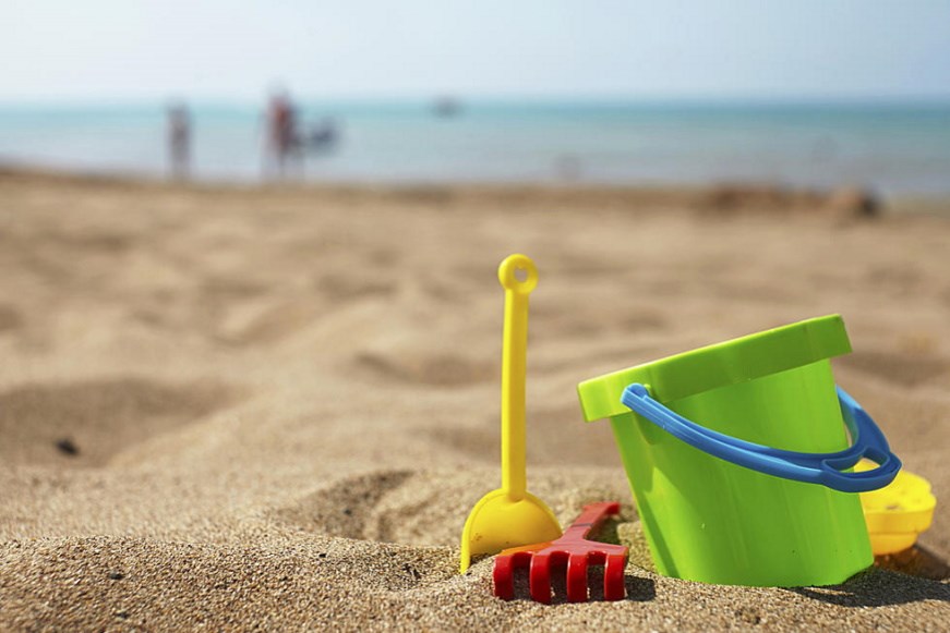 A bucket and spade sitting on a beach with the sea in the background