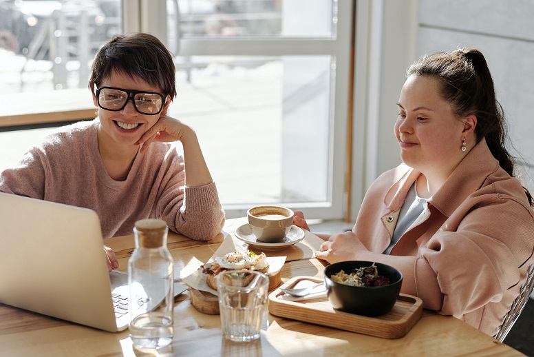 Girl and woman looking at laptop while having lunch