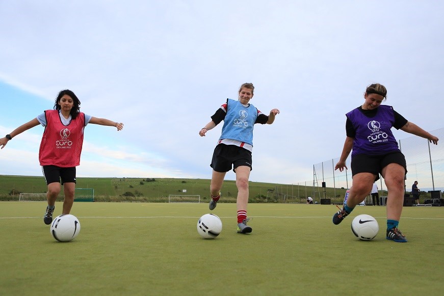 Three women kicking footballs