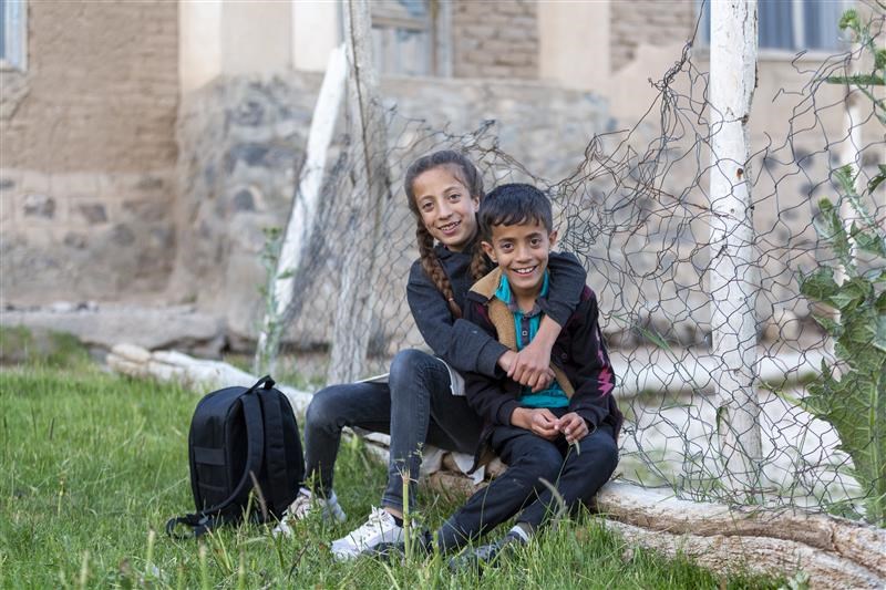 Two children sitting next to a broken fence