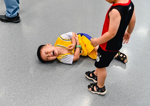 A child standing over another crying child