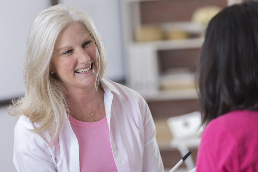 A woman smiling at another person who is holding a pen