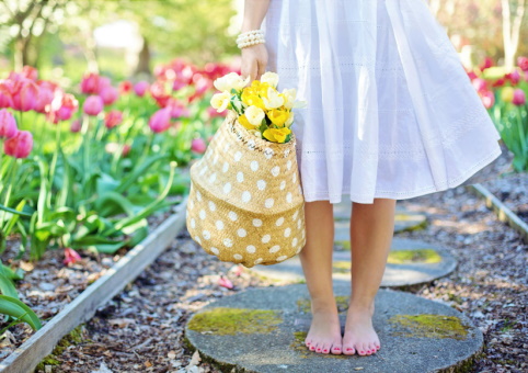 A girl standing on a path surrounded by, and carrying, flowers