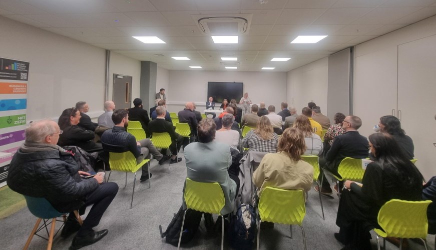 Attendees at the meeting, sitting on chairs, listening to the Leader of the Council speaking. There are about 30 people