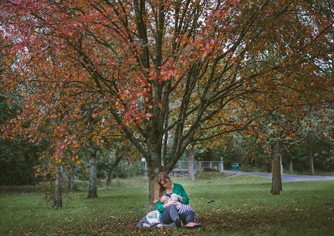 A woman feeding her baby beneath a tree