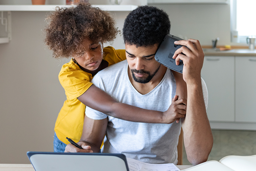 A man looking concerned about paperwork while being hugged by a child