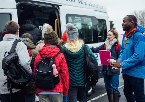 Two adults supervising children who are boarding a minibus 