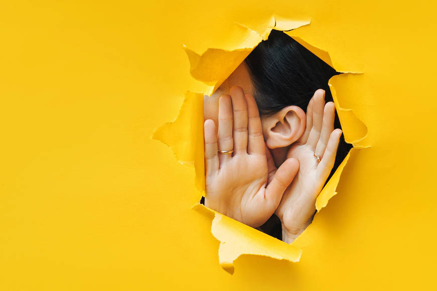 A hole in a large paper sheet showing someone cupping their ear so as to better hear you