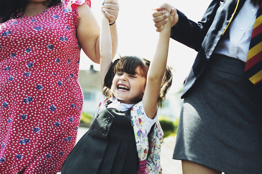 Smiling little girl holding hands of mum and older schoolgirl