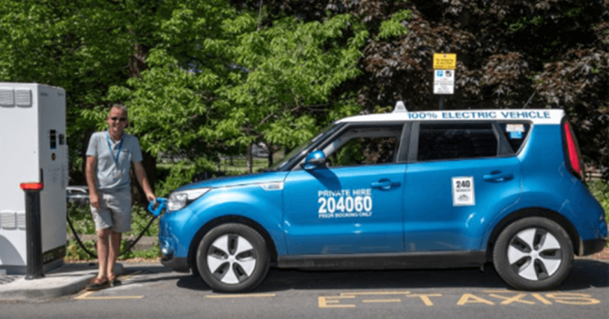 A taxi driver plugging in an electric taxi to a public charge point