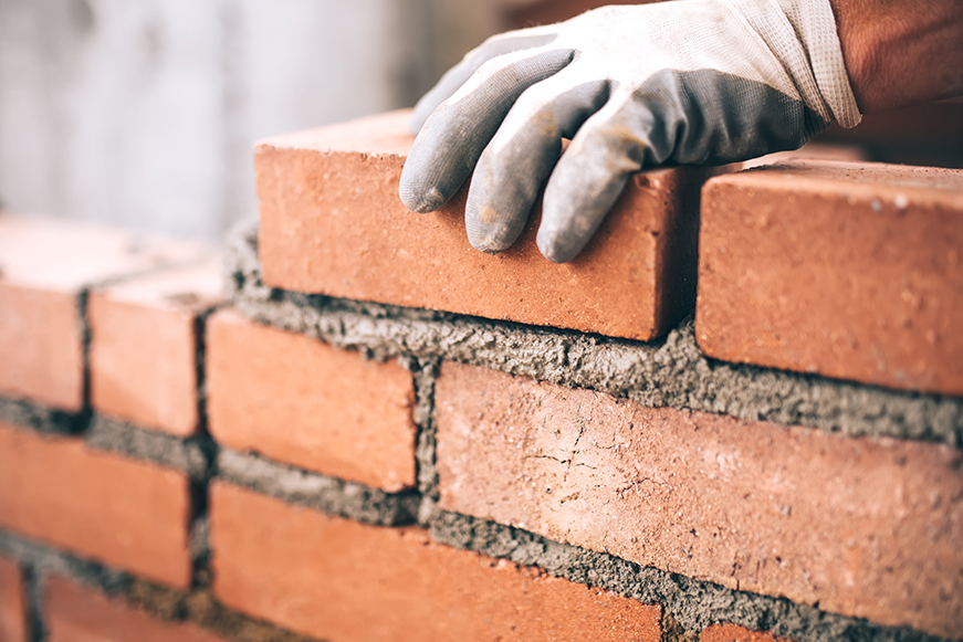 A gloved hand placing a brick on a wall