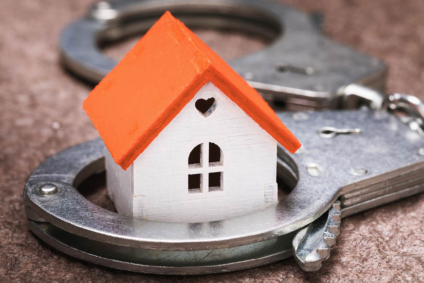 A small wooden house model within one cuff of a pair of handcuffs