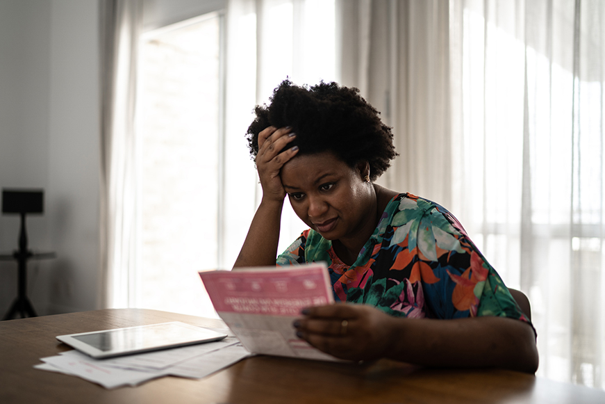 Woman Sat At Table With Head In Her Hands Looking Worried Holding A Bill