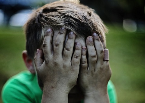 A boy covering his face with his hands