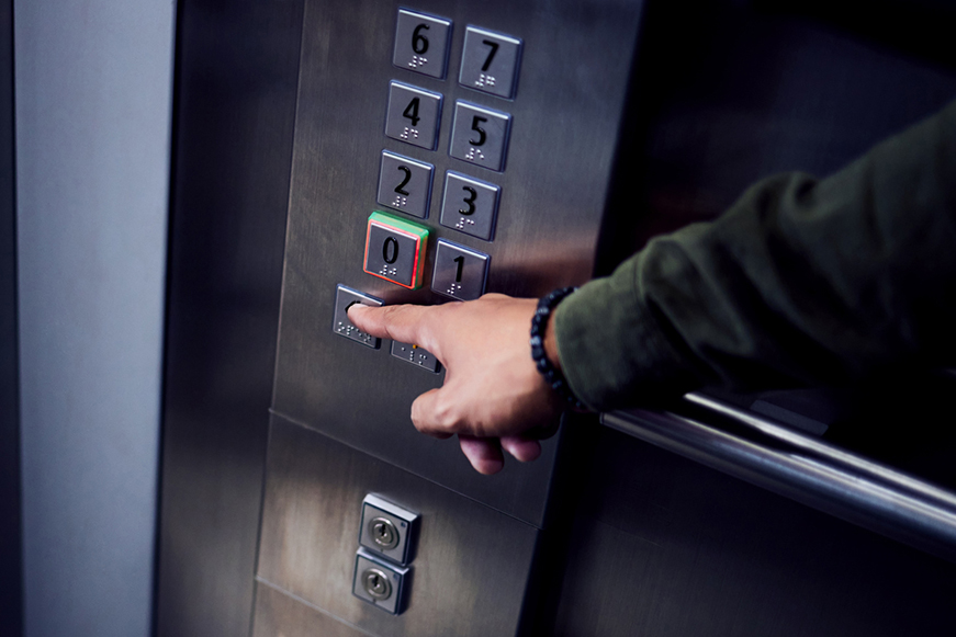 A lift control panel with a hand pressing one of the buttons