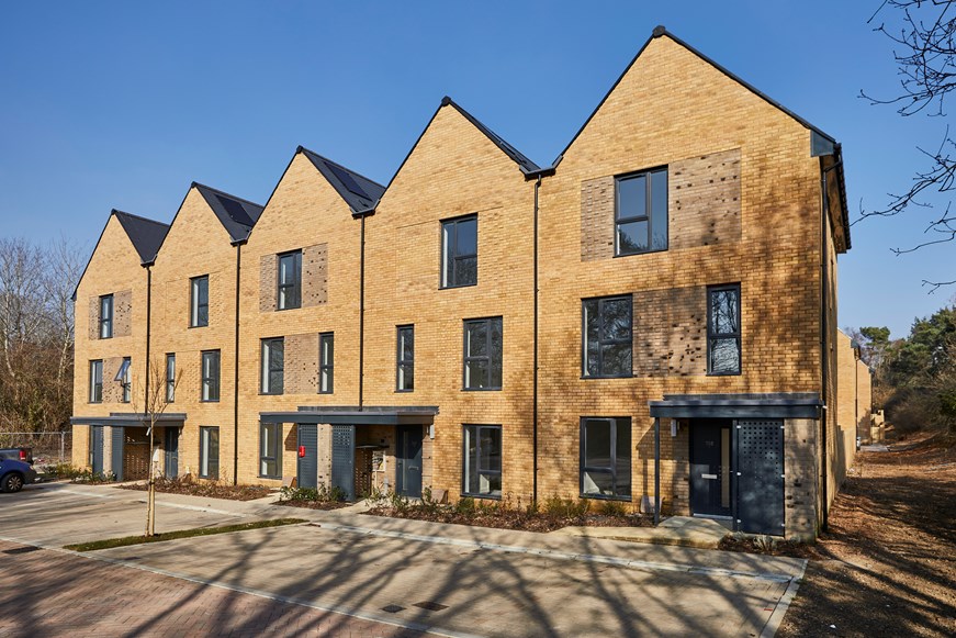 Image of five brown brick buildings with black windows and black doors on a sunny day