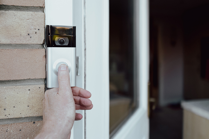 A thumb pressing a video doorbell A thumb pressing a video doorbell